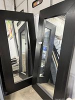 Black floor mirror with wide black wooden frame leaning against a wall, visible scrapes on frame.