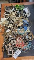 Full view of mixed costume jewelry on wooden table featuring various bracelets, necklaces, earrings, and bangles in multiple colors and styles.