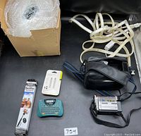 Overview photo showing boxed disco ball, coiled LED light strip, black camcorder case, label printer, selfie stick in package, and small white electronic accessory.