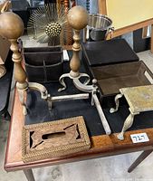 Wide view of the lot showing multiple home decor items on a wooden table, including andirons, a carved wooden box, leather storage box, glass tray, and metal stand.