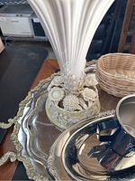 Photo showing white ceramic vase with floral relief base on silver serving tray with wicker basket in the background