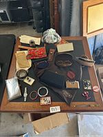 Photo showing all items spread on a table including gloves, camera, red floral purse, eyeglasses in a case, watch, bracelets, and small cases
