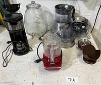 Full shot of lot including Kenwood food processor with attachments, KitchenAid blender base, Sboly coffee grinder, glass beverage dispenser, and other accessories arranged on surface.