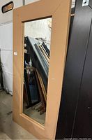 Full view of large tan framed stand up mirror showing rectangular shape and reflection.