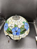 Full view of the lamp showing blue flower stained glass shade and dark metal base.