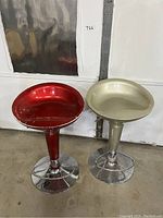 Two vintage barstools, one red and one beige, showing seats and bases side by side against a white wall.