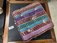 Top view of a square vintage floor cushion showing colorful hand-embroidered stripes with metallic thread and tassels on edges.
