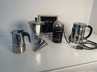 Front view of all items including coffee makers, coffee grinder, and funnel on white surface