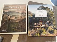 Front covers of two travel-themed coffee table books titled 'The Journey' and 'Great Escapes Africa' laid flat on a surface.