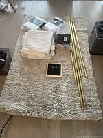 Photo showing gold-colored curtain rods and finials, along with gray linen curtain panels and a gray shag rug beneath.