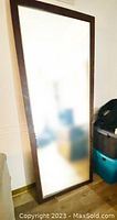 Full height floor mirror leaning against wall, shows entire reflective surface and dark wood frame.
