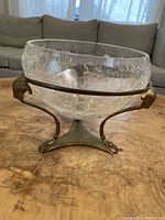 Full view of the crackle glass bowl supported by a brass stand featuring three ram's head decorations as legs.