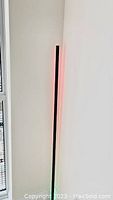Shows tall black LED corner lamp fitted into a room corner, vertical segment lit with red light.