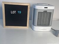Photo of the white Lasko small portable heater alongside a wooden-framed letter board showing LOT 19