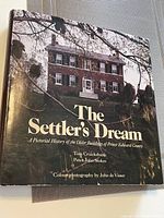 Front cover of first edition book 'The Settler's Dream' showing an old brick building with trees and the title text.