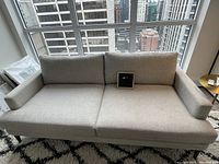 Front facing view of West Elm Andes sofa in storm grey chenille tweed, showing two loose back cushions, one bench seat cushion, and black tapered wooden legs on patterned rug