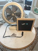 White Vornado table top fan placed on a white marble effect table with a sign 'LOT 18'