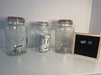 Photo showing two large glass water jugs styled as Mason jars, each with a metal spigot, and one large Mason jar with flip-top lid.