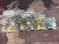 Four plastic bags of assorted metal Monopoly game pieces and coins in various silver and gold colors