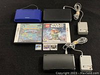 Two Nintendo DS consoles (blue and black), DS game case, 3DS game case and three power adapters