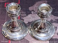 Photo showing both silver candle stick holders resting on a map-patterned surface.