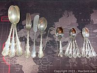 Six tablespoons, one soup spoon, three dessert spoons, four teaspoons, one salad fork and one butter knife on map background