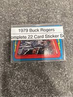 Plastic case containing complete 22-card 1979 Buck Rogers sticker set showing front label with colorful sticker art