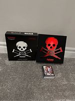 Photo showing two Jackass collectible trading card box sets and one deck of Jackass trading cards on carpet against white wall.
