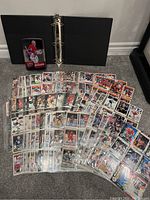 Black 3-ring binder opened with numerous hockey cards spread out in front laid on carpet.