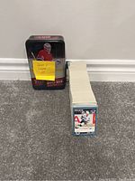 Metal tin with 2015-16 Upper Deck Series 2 hockey card set and large stack of 1992-93 Score hockey cards stacked next to it on carpeted floor.