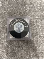 Photo of the hockey puck showing the Toronto Maple Leafs logo and the silver signature of David Keon with #14 on the top.