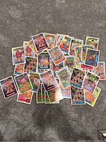 Scattered assortment of 37 Trash Can Trolls trading cards on a gray carpet.