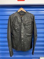 Front view of black leather motorcycle jacket on hanger against blue background