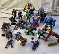 Full assortment of varying superhero and action figures displayed on white surface with beige cloth background, showing their poses and details.