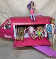 Pink Barbie airplane with door open and four dolls posed around and inside plane