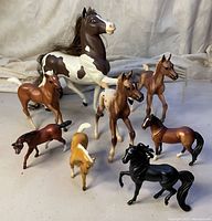 Eight horse figurines arranged on a surface including one large black and white horse and seven smaller horses in various colors.