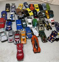 Photo of assorted die cast toy vehicles arranged in rows on a white surface.