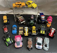 Top view of 18 die-cast toy vehicles including yellow taxi, yellow VW beetle, monster trucks, race cars, and construction vehicles.