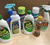 Photo of various household cleaning product bottles including Soft Scrub Bleach Cleanser, Wilbert Lemon Oil, Drachelle aerosol spray, and other spray bottles.
