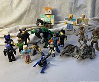 Various toy figures including block-style Minecraft and Roblox characters, plus yellow skeleton-like and armored figures with two dinosaur models in front