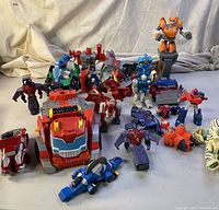 Multiple transforming toys of various colors including red, blue, orange, purple, and white. Includes whole figures and parts in an unorganized layout.