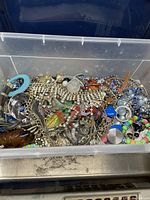 Plastic bin filled with assorted broken jewelry parts including rhinestone chains, colorful beads, metal rings, and clasps.