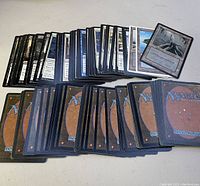 Front and back views of a large assortment of Magic The Gathering cards spread out on a flat surface, showing card illustrations and card backs.