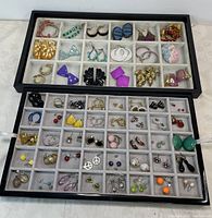 Top-down view of two trays with multiple pairs of vintage, retro, modern earrings including hoops, studs, dangles in various colors and styles.