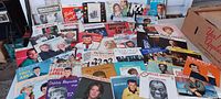 Photo showing a wide assortment of colorful 45 RPM record sleeves from various well-known mid-20th century artists arranged on a table.