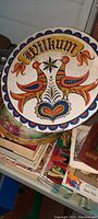 Full view of circular antique hex sign showing vibrant stylized birds, floral motifs, and "Willkum" text on Masonite.