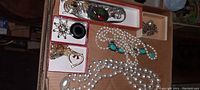Overall view of pearl necklaces, black onyx-style pendant, silver-tone filigree brooch, and heart pendant arranged in boxes