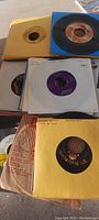 Top view of several 45 RPM records partially out of their sleeves showing labels and some with handwritten markings.