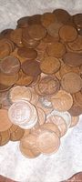 Close-up photo showing a pile of copper-colored wheat pennies with the reverse design visible with 'One Cent' and wheat stalks, coins vary in patina and wear.