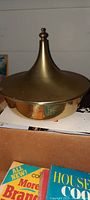 Photo of the top half of the vintage Art Deco serving dish with a goldtone conical finial lid and round body.